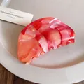 Detailed view of a marbled red and orange acrylic hair claw clip on a beige plate - Oval Hair Claw / Orange