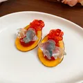 Close-up of resin koi fish and rose earrings on a white plate - Red & White