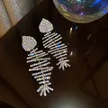 Primo piano di orecchini a lisca di pesce con strass su una superficie scura riflettente - Forma a Lisca di Pesce / Oro