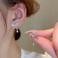 Primo piano di orecchini a fiocco in argento con pendente a cuore e cristalli luminosi. - Pendaglio Cuore con Fiocco / Argento