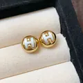 Detailed close-up of gold-plated round stud earrings featuring a white H logo design - Letter H Style / Gold
