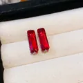 Close-up detail of elegant rectangular red zircon stud earrings on beige display cushion - Large / Red