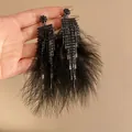 Close-up of elegant black feather tassel earrings with sparkling rhinestone fringe detail. - Black
