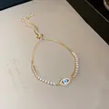 Close-up of gold adjustable bracelet with sparkling zircons and blue evil eye motif. - Adjustable Drawstring / Gold