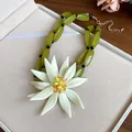 Close-up of olive green beaded necklace featuring a large white 3D floral pendant. - Necklace / White