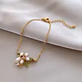 Detailansicht eines goldfarbenen Armbands mit weißer Emaille-Blume und grünen Zirkonia. - Armband / Gold-Weiß