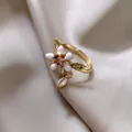 Makroansicht eines vergoldeten Rings mit weißer Emaille-Blume und grünen Zirkonia-Blättern - Ring / Gold-Weiß