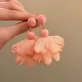 Macro detail of sweet peach pink raffia flower drop earrings featuring fabric petal tassels - Pink
