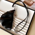 Close-up of a black faux leather croissant-shaped coin purse necklace accessory. - Black
