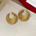 Detailed close-up view of elegant gold textured hollow hoop earrings on a beige fabric - Small / Gold