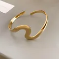 Detail showing the polished finish and unique wavy design of a gold open cuff bracelet - Gold