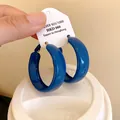 Macro view of Klein blue minimalist spray-painted hoop earrings shown on a white tag - Silver Post - Blue - Wide Surface - 39mm Diameter