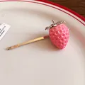 Detail shot of a cute pink resin strawberry hair clip resting on a white ceramic plate. - Strawberry Hair Clip