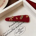 Dettaglio macro della molletta in feltro rosso con ciondoli a forma di cavallo e monete - Clip BB Rosso Elementi di Ricchezza