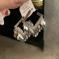 Close-up of silver hoop earrings with dangling leaf tassel charms and price tag. - Square Tassel Silver Post Style (Silver Post)