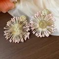 Close-up detail of bohemian raffia flower earrings with gold metal and pink seed buds - Gold-Pink