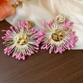 Macro view of oversized raffia flower earrings with hammered gold metal and pink accents - Gold-Rose Red