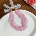 Primo piano di una dolce collana di perline rosa multifilo con fiocco in pizzo bianco. - Viola