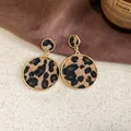 Gros plan de boucles d'oreilles rondes rétro imprimé léopard avec bordure dorée sur tissu marron. - Grand (15#)