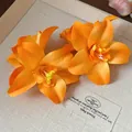 Vue détaillée de deux pinces à cheveux en fleurs de tissu orange sur un support en lin. - Pinces à cheveux bec de canard / 1 Pièce / Orange