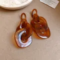 Macro detail of amber-colored acrylic geometric chain link earrings with warm tones. - Amber Style