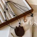 Detailed macro view of dark brown leather pouch pendant on a black beaded necklace cord - Dark Coffee