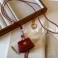 Close-up of red leather mini bag pendant necklace with gold button on long cord - Burgundy