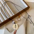 Close-up view of a geometric silver pendant on a black leather cord over a magazine. - Black-Silver