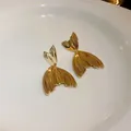 Close-up of elegant gold-tone fishtail drop earrings with textured surface detail. - Large Fishtail Studs / Gold