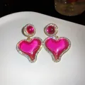 Gros plan détaillé de boucles d'oreilles cœur rose avec strass et bordure dorée. - Rose