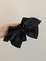 Vista dettagliata di una grande molletta per capelli in raso nero con fiocco tenuta in mano - Pinza per capelli / Nero