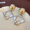 Macro view of geometric dangle earrings with shiny gold spheres and silver accents - Gold