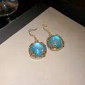 Close-up of vintage gold-tone hook earrings featuring a glowing blue resin centerpiece. - Earring Hooks / Gold Blue