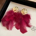 Detail of oversized burgundy red feather tassel earrings with hammered gold-tone metal top - Stud Style (HE29175) / 925 Silver Needle / Red