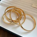 Gros plan élégant d'un ensemble de bracelets joncs circulaires en métal doré brillant - Rond Lisse / Lot de 5 / Or