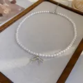 Elegante weiße Perlenkette mit einem zarten silbernen Schleifenanhänger auf einem Displaybrett - 42# Halskette-Schleife