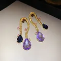 Close-up macro view of vintage braided gold earrings with purple teardrop crystals. - Gold