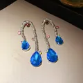 Close-up of vintage woven silver earrings featuring vibrant blue water drop stones. - Silver