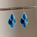 Detailed view of translucent blue teardrop oil-dripped earrings with gold hooks. - Hook Style / Blue