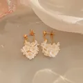 Dettaglio di eleganti orecchini a grappolo di fiori di perla bianca con catene d'oro. - Oro