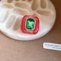 Detail view of a vintage red resin ring featuring a large emerald green center gemstone. - Pink and Green