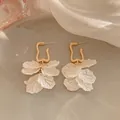 Dettaglio macro di eleganti orecchini a fiore dorati con petali bianchi testurizzati - Oro-Bianco