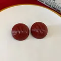 Macro view of vintage-style round dark red earrings featuring a textured ribbed design. - Striped / Red