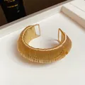 Macro view of a gold metallic woven open cuff bracelet showing fine wire texture. - Gold