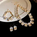 Nahaufnahme des Schmucksets mit klaren Kristallen im Smaragdschliff und goldenem Finish. - Halskette + Armband + Ohrringe 3-teiliges Set / Weiß
