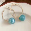 Close-up view of gold-tone hoop earrings featuring smooth teal resin spherical beads. - Blue
