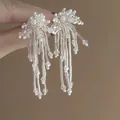Primer plano de pendientes hechos a mano con flores de cuentas blancas y borlas finas - Blanco (7#)