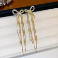 Macro view of elegant 18k gold plated bow earrings featuring sparkling zircon tassels. - Bow Tassel / Gold