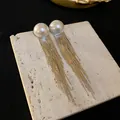 Detailed shot of elegant long gold tassel earrings with white pearls on a stone base - Silver