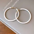 Close-up detail of white leather wrapped round hoop earrings with golden minimalist accents - White